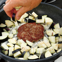 肉の片面に十分な焼き色がついたら裏返し、まわりに玉ねぎ、なすを加え、肉汁を吸わせながら炒める。