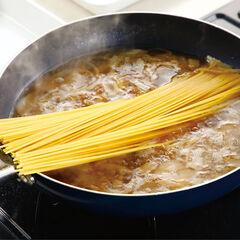 フライパンの中の水分が沸騰したら弱めの中火にして、スパゲッティの片側が沈むように入れる。１分程度おいてスパゲッティが柔らかくなったら曲げるようにして全体を浸してから、強めの中火で茹でる。